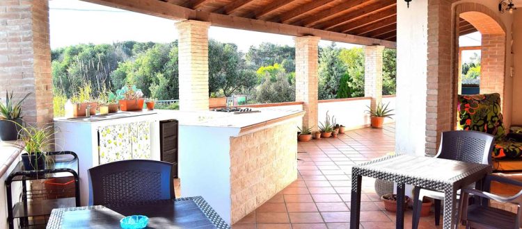 Ampia veranda esterna con cucina in muratura, tavolo da pranzo, sedie e area relax