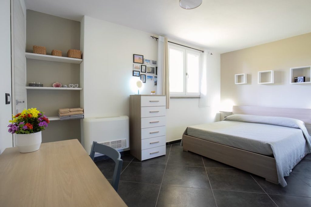 Stanza chiara e moderna con letto matrimoniale, scrivania in legno, cassettiere e pavimento antracite