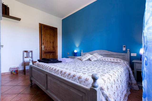 Camera matrimoniale rustica con parete blu mare Camera matrimoniale con pareti blu mare, letto matrimoniale e due lampade da comodino